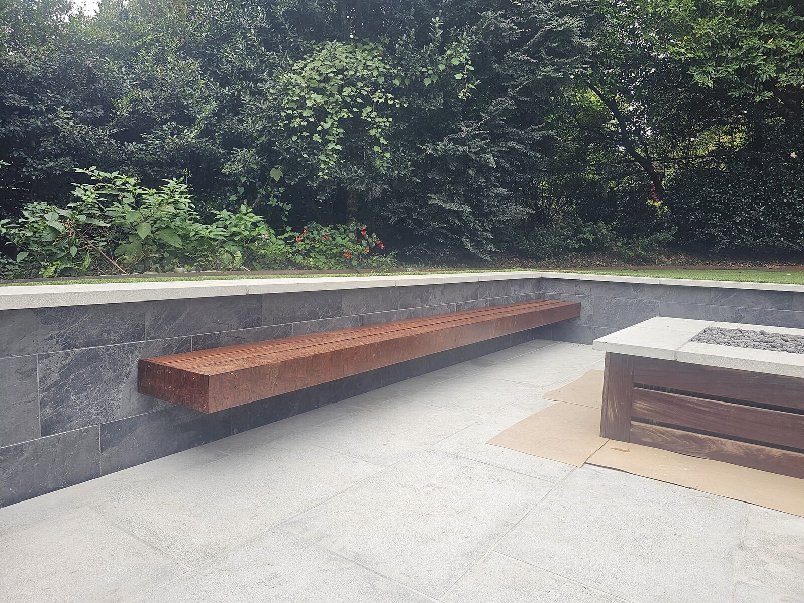Close detail of the floating Ipe bench with concealed fasteners, mounted against the dark stone-veneer wall