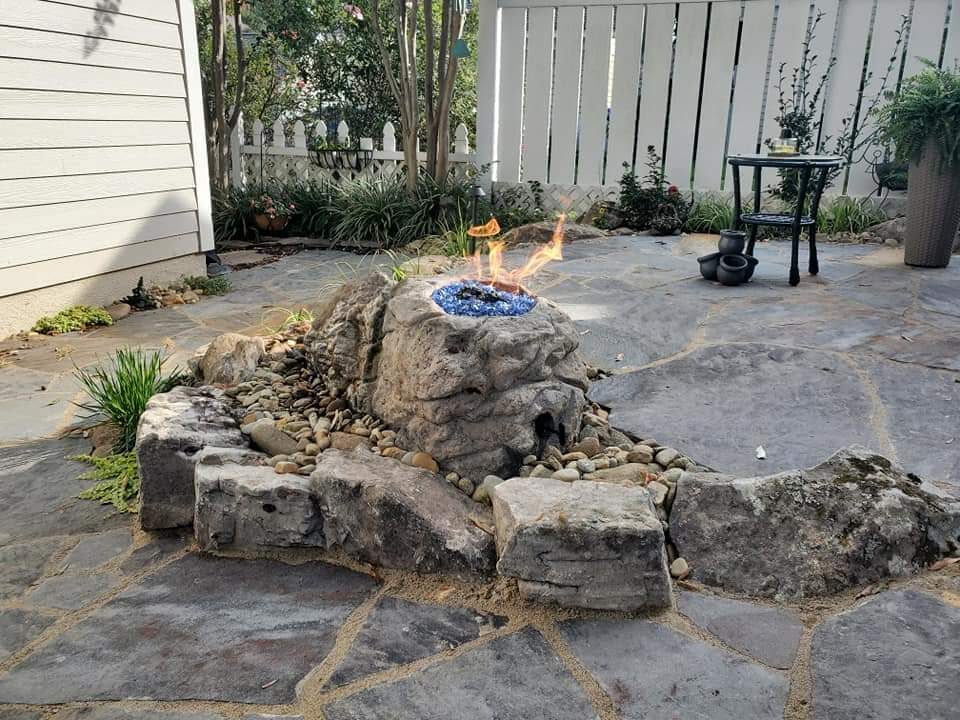 A flagstone patio with a carved boulder gas fire feature surrounded by river rock