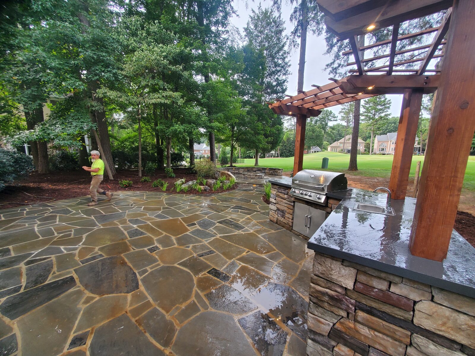 A flagstone patio with a timber pergola over a stone-faced outdoor kitchen and grill
